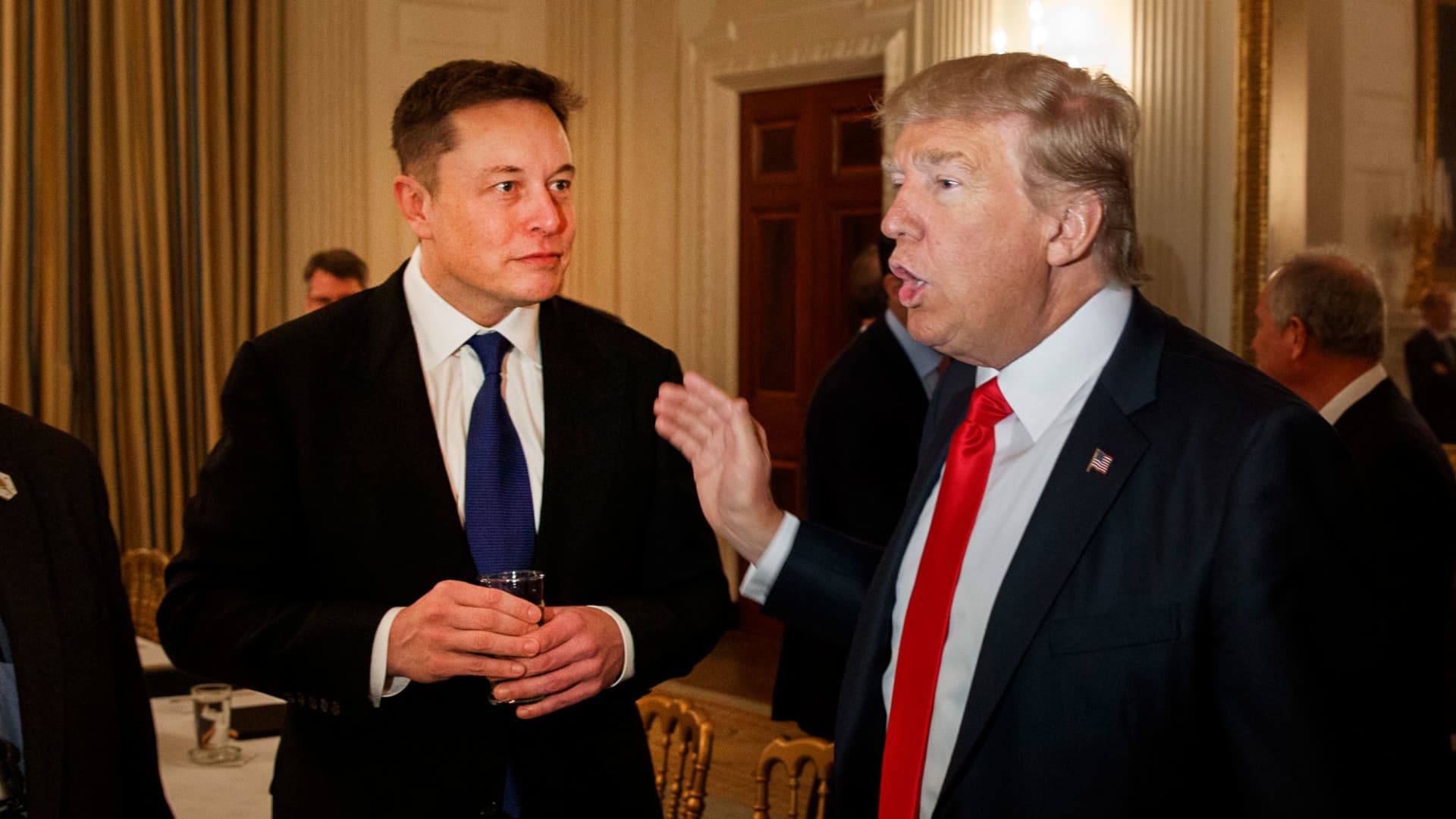 "Elon Musk and Donald Trump talking at an event, with Musk speaking and Trump listening."

