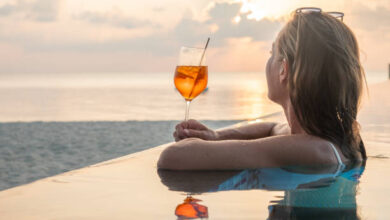 A woman enjoying a cocktail by the sea, gazing at the sky, embracing the luxury and elegance of the SLS Lifestyle.