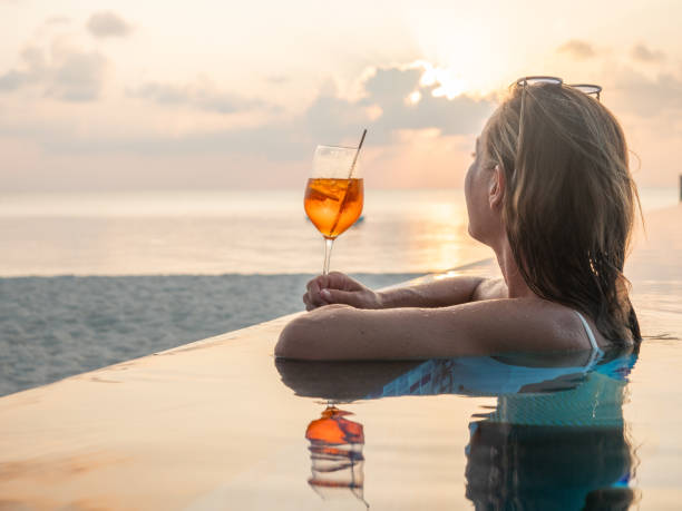 A woman enjoying a cocktail by the sea, gazing at the sky, embracing the luxury and elegance of the SLS Lifestyle.